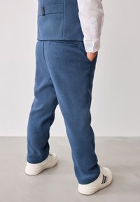 Pantalones texturizados azules con un corte relajado, que cuentan con bolsillos laterales y un diseño elegante, combinados con zapatillas blancas y acentos sutiles.