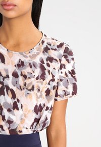 Top a maniche corte con una stampa animale astratta multicolore in tonalità di marrone, grigio e beige, con scollatura rotonda e tessuto morbido.
