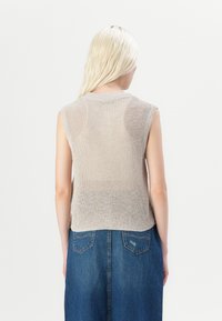 Beige strikket ærmeløs topp med en teksturert overflate, med rund hals og sidespalter, brukt sammen med et blått denimskjørt.