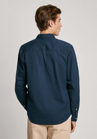 Camisa de manga larga azul marino de tela de algodón con yugo trasero, puños con botón y dobladillo curvado, que presenta una textura suave y un cuello clásico.