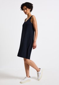 Abito nero a coste senza maniche con scollatura a V, caratterizzato da una silhouette morbida e che arriva appena sopra il ginocchio. Le sneakers bianche completano il look.