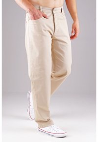 Beige Baumwollhose mit geradem Bein, Fronttaschen und Reißverschluss. Getragen mit weißen Sneakers mit roten und blauen Akzenten.