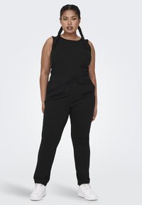 Black sleeveless top paired with black tapered pants featuring an elastic waistband and drawstring. White sneakers complete the outfit.
