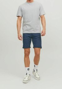 Szaro-biała koszulka w paski połączona z ciemnoniebieskimi krótkimi spodniami. Całość dopełniają białe sneakersy oraz białe skarpetki z czarnymi akcentami.