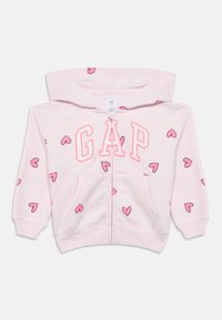 Ανοιχτό ροζ φούτερ με εμπρός φερμουάρ, με μεγάλο λογότυπο "GAP" και μικρές ροζ καρδιές ως επαναλαμβανόμενο μοτίβο. Μαλακή υφή υφάσματος.