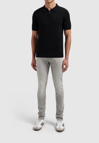 Zwarte polo met korte mouwen en ritskraag, gecombineerd met lichtgrijze slim-fit jeans en witte sneakers met zwarte strepen.