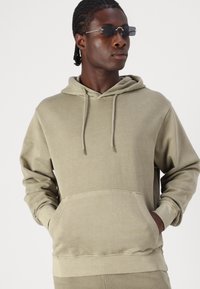 Lys oliven grøn hoodie lavet af blødt stof, med en frontlomme, snoretræk i hætten og ribbede manchetter, i en afslappet pasform.