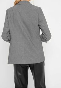 Blazer à motifs noir et blanc avec des manches longues et une coupe ajustée. Tissu lisse, revers crantés, sans fermetures visibles, et silhouette structurée.