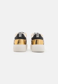 Svarte og gull sneakers med teksturert gull hæl, hvit såle og svart stoffoverdel med et distinkt logo på hæltabben.