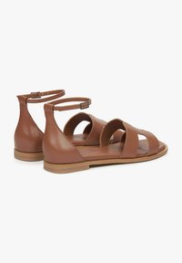 Bruine leren sandalen met een platte zool, voorzien van meerdere gekruiste banden en een sluiting met gespsluiting rond de enkel. Soepele textuur en open ontwerp.