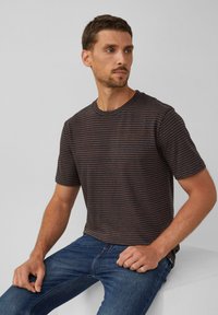 Camiseta de manga corta a rayas en azul oscuro y óxido, hecha de tela suave, diseño con cuello redondo, combinada con jeans de mezclilla azul, en postura sentada.