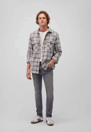 Gray plaid flannel shirt with two chest pockets, paired with gray jeans and white sneakers featuring black stripes. Plain white T-shirt underneath.
