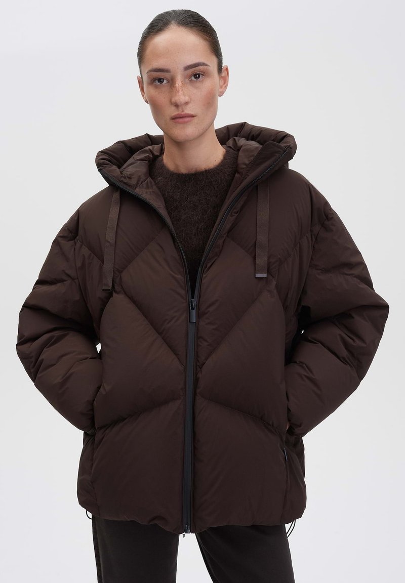 Giacca a vento marrone con design trapuntato, chiusura con zip e cappuccio oversize. Caratterizzata da cordini regolabili e tasche laterali.