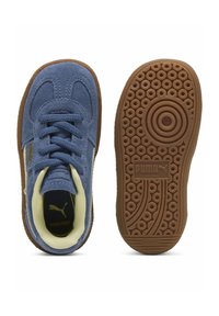 Blåmocka sneakers med en texturerad gummisula, rundade mönster, och en gul accent på det inre foderet; har snören och varumärkeslogotyp.