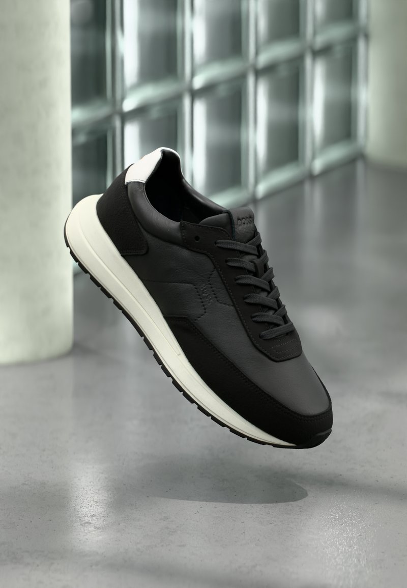 Baskets en cuir noir à texture lisse, semelle blanche et accent de talon contrastant. Elles présentent des lacets ronds et un profil épuré.