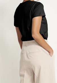 Sort kortærmet skjorte kombineret med beige højttaljede bukser. Skjorten har en glat tekstur; bukserne har dobbelte baglommer.