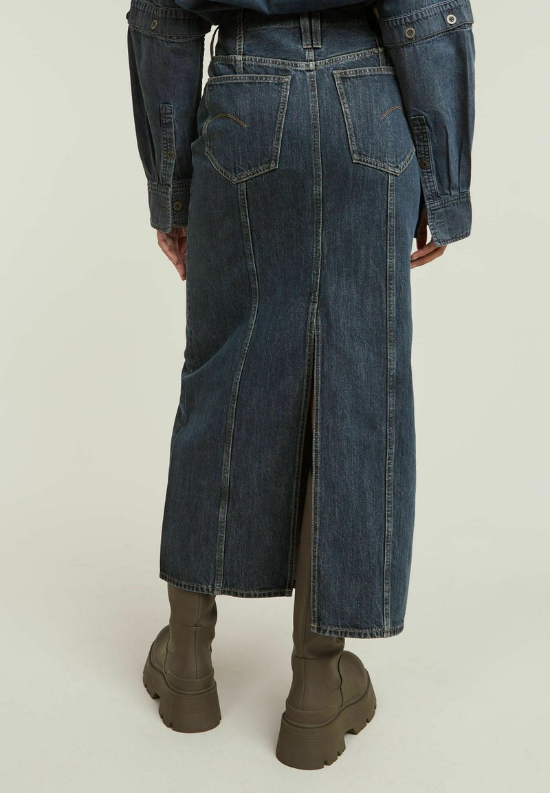 Dunkelblaue Denim-Maxiröhre mit einem mittigen Schlitz. Verfügt über zwei hintere Taschen und eine figurbetonte Taille, kombiniert mit olivgrünen, kniehohen Stiefeln.