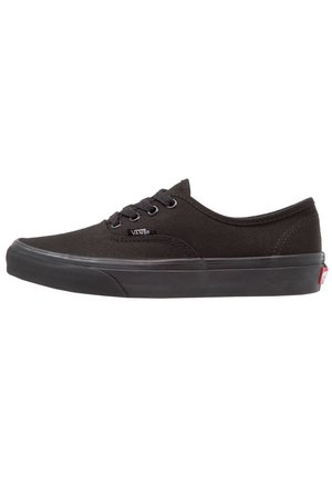Baskets basses en toile noire avec design à lacets, semelle en caoutchouc et étiquette logo Vans sur le côté ; texture lisse et style minimaliste.