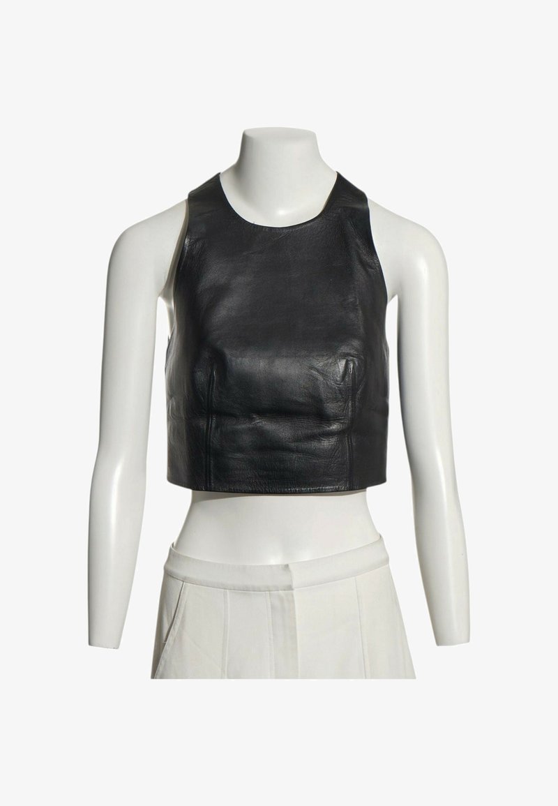 Top court sans manches en cuir noir présenté sur un torse de mannequin blanc portant un pantalon blanc taille haute.