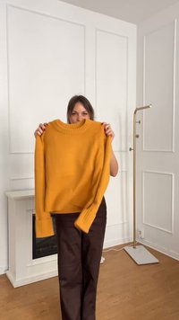 Senfgelber Pullover mit einem gerippten Kragen und Bündchen, gefertigt aus einem weichen, strukturierten Stoff, vor einem hellen Hintergrund gehalten.