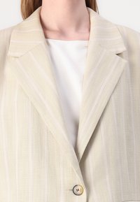 Beige gestreepte blazer met een gestructureerd ontwerp, voorzien van een hals met klep en een enkele knoopsluiting. Zachte, geweven stof.