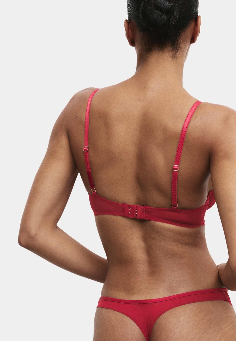Czerwony zestaw bielizny z cienkimi ramiączkami, zapięciem na haftki i dopasowanym stringiem. Tkanina wygląda na gładką z delikatnym połyskiem.