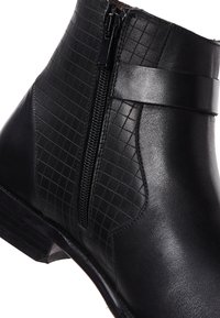 Bottine noire avec un motif quadrillé texturé sur un côté, finition en cuir lisse, fermeture éclair latérale et petit talon empilé.