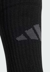 Calcetín atlético negro con textura acanalada, que presenta un diseño de logotipo gris cerca de la parte superior. El tejido parece elástico y duradero.