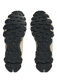 Svarta gummisulor har djupa, robusta mönster för grepp, med en ljus tan-färgad kant runt kanterna och texturerade ytor.