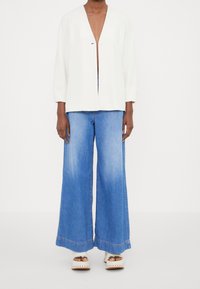 Vit kavaj med v-igång och en enda knappstängning, kombinerad med vida ljusblå denimjeans med en något urtvättad finish och fransad nederkant.