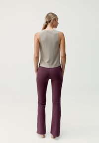 Canotta in tessuto grigio chiaro con dettaglio posteriore perforato abbinata a pantaloni fitted svasati in bordeaux scuro.