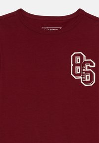 Bordeaux katoenen t-shirt met een ronde halslijn, voorzien van het witte blokcijfer "86" en de tekst "FRIBOO" op de voorkant. Zachte textuur.