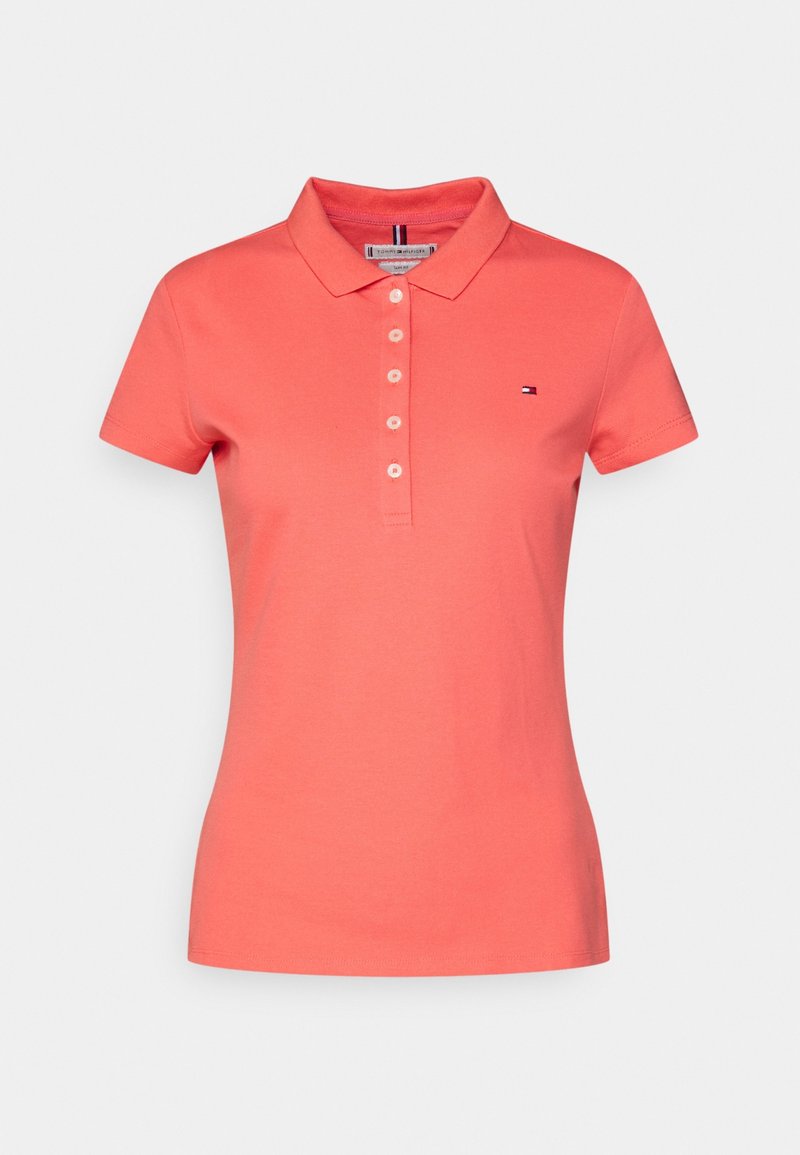 Kaos polo berwarna koral terbuat dari katun. Memiliki plaket tiga kancing, lengan pendek, dan logo kecil di dada. Desain potongan klasik.