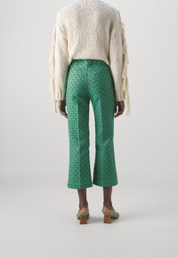 Gröna mönstrade utsvängda byxor med diamantdesign, i kombination med en texturerad krämfärgad tröja och  öppettåade klackar. Detaljer med träklackar syns tydligt.