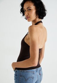 Top halter maro cu un design ajustat, având un decolteu rotund și spate deschis. Asortat cu blugi din denim de un albastru deschis, cu talie înaltă.