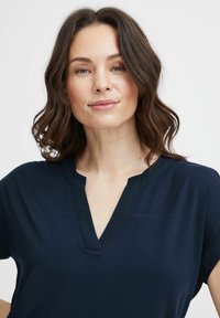 Top blu navy a maniche corte con scollatura a V, tessuto morbido e bordino nero a contrasto attorno allo scollo.