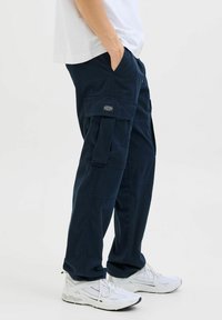 Marinblå cargobyxor med flera fickor, avslappnad passform och slitstarkt tyg. Kombinerade med vita sportskor för kontrast.