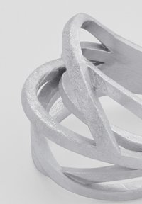 Bracciale in metallo argento con anelli intrecciati e finitura texturizzata, che evidenzia forme lisce e curve in un design moderno.