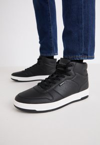 Sneaker alte nere in pelle testurizzata, con lacci neri, suola in gomma bianca e un piccolo logo sul lato.