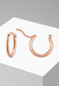 Orecchini a cerchio in oro rosa con un design sottile e una texture liscia. Un orecchino è un cerchio tradizionale, l'altro ha un contorno ondulato.