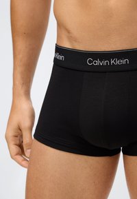Černé bavlněné trenýrky s širokým elastickým pasem, na kterém je bílý nápis "Calvin Klein". Hladký povrch a přiléhavý střih.