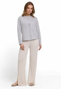 Cardigan grigio chiaro con bottoni e maniche lunghe, abbinato a pantaloni crema a gamba larga con texture che presentano un motivo a coste e spacchi alla caviglia.