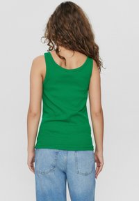Grön ärmlös t-shirt med rund halsringning, tillverkad av mjukt bomullsmaterial. Matcher med ljusblå denimjeans.