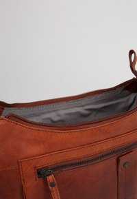 Brązowa skórzana torba z zamkiem błyskawicznym. Wnętrze ma czarno-białą w kratkę podszewkę. Z przodu znajduje się mała kieszeń na zamek.