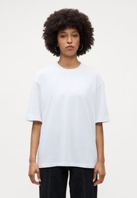 Balta per didelį T-shirt su trumpomis rankovėmis, apvaliu iškirpimu, pagaminta iš medvilnės. Švelni tekstūra, minimalus dizainas, jokių matomų raštų ar akcentų.
