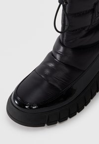 Must musta ankle boot, millel läikiva patendi varvasetipu, tekstureeritud kummist talla ja nööpide detailiga. Pehme, särav materjal koos tugeva disainiga.