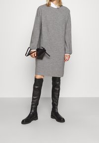Robe en maille grise à manches longues et col rond, associée à des bottes en cuir noires au-dessus du genou et un petit sac à main noir.