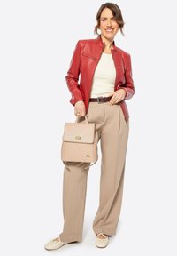 Rote Leder-Jacke mit Reißverschluss, cremefarbenes Oberteil, beigefarbene weite Hose, hält einen hellbeigen Rucksack mit Druckverschluss und goldenen Hardware-Akzenten.