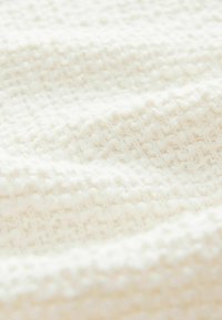 Tissu texturé blanc, présentant un motif tissé avec des boules en relief, créant une surface douce et tactile avec une apparence confortable.