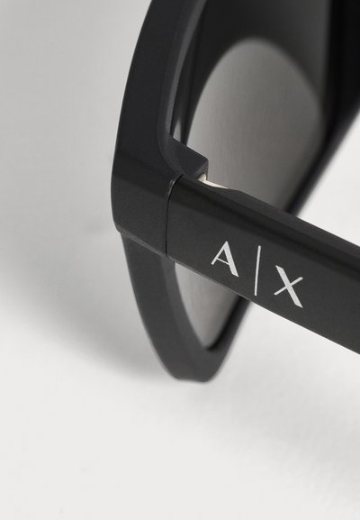 Gros plan sur des lunettes noires avec le logo A|X imprimé sur la branche, sur un fond clair.